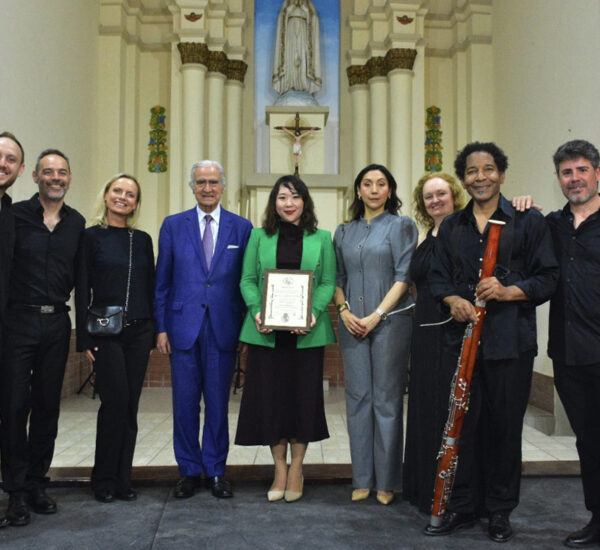 Group of nine people in formal attire posing with a framed certificate inside a church sanctuary with an altar in the background.