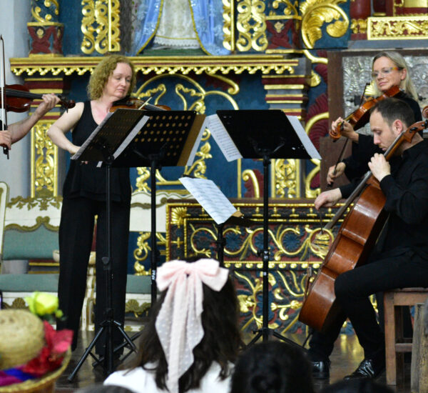 String quartet performing on a stage in a richly gilded, ornate hall with audience watching in the foreground.
