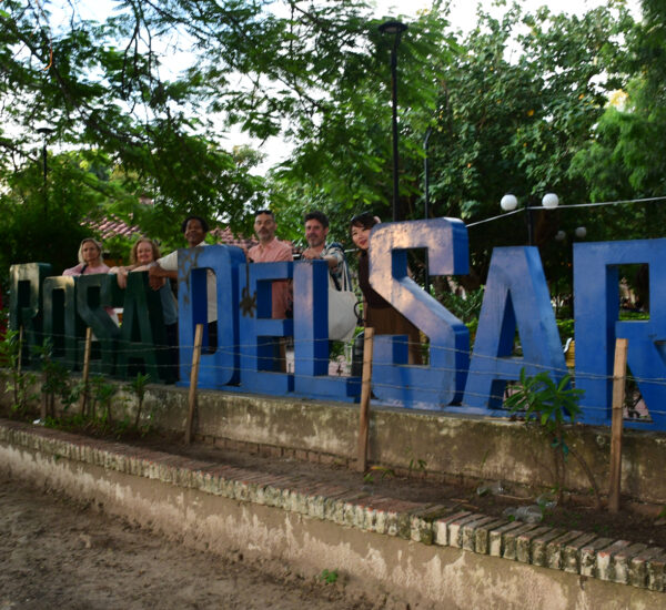 Group of people posing behind large, colorful letters in a green outdoor park.