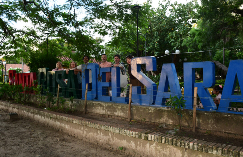 Group of people posing behind large, colorful letters in a green outdoor park.