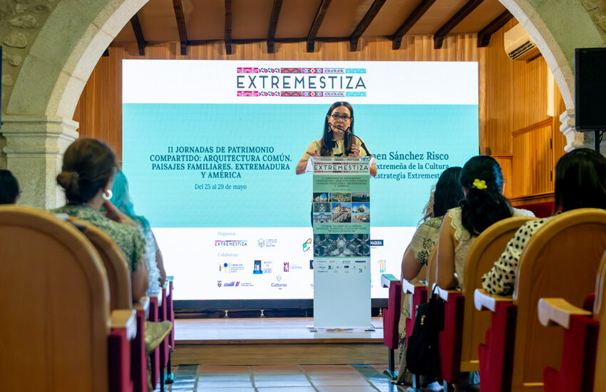 Woman speaks at a conference podium on a stage with a large EXTREMESTIZA banner and blue screen behind her; audience seated in a hall.