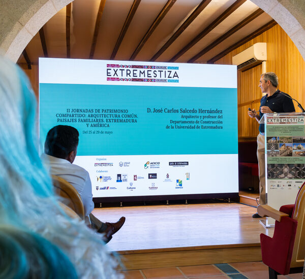 Speaker at a lectern on a stage, presenting beside a large screen that says EXTREMESTIZA.