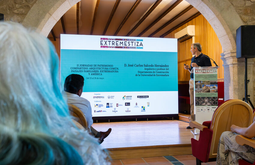 Speaker at a lectern on a stage, presenting beside a large screen that says EXTREMESTIZA.