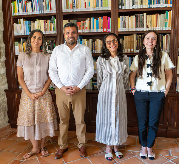 Four adults stand side by side in a library, smiling with tall bookshelves behind them.