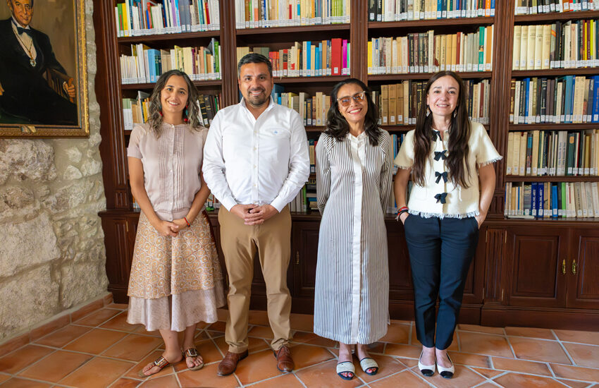 Four adults stand side by side in a library, smiling with tall bookshelves behind them.