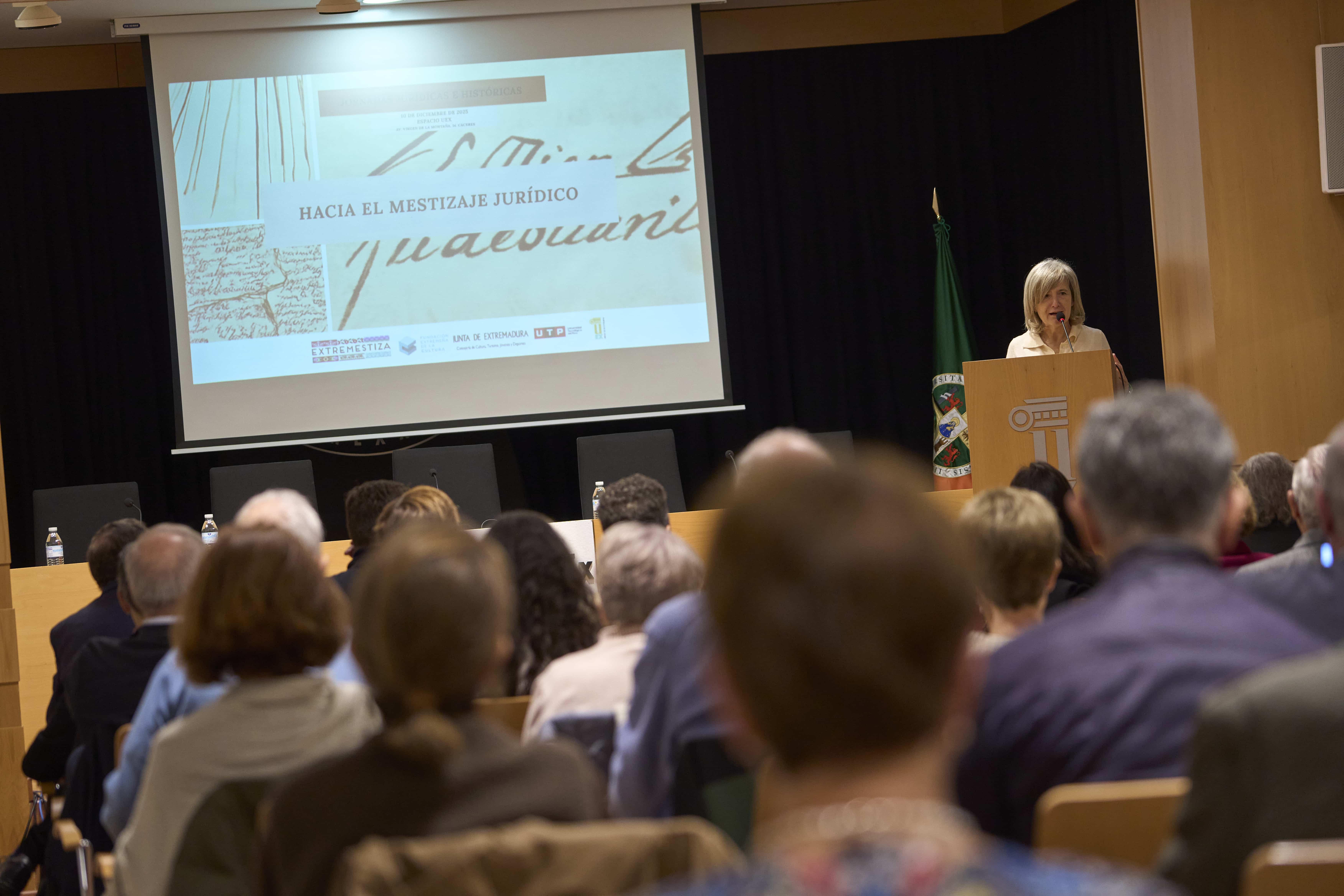 Woman at a podium presenting to an audience; slide on screen reads 'HACIA EL MESTIZAJE JURÍDICO'.