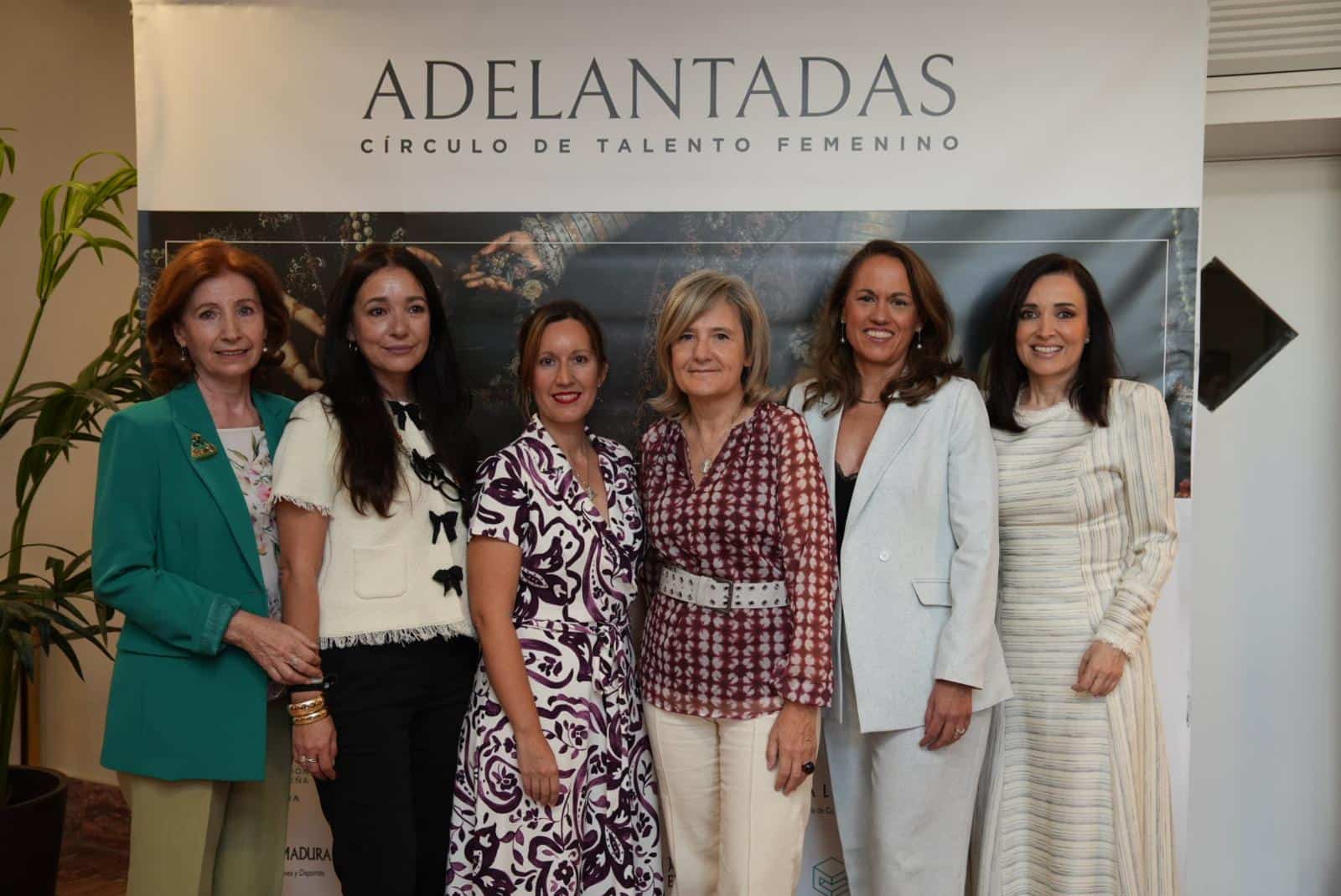 Six women posing together at an event in front of a banner that reads ADELANTADAS.